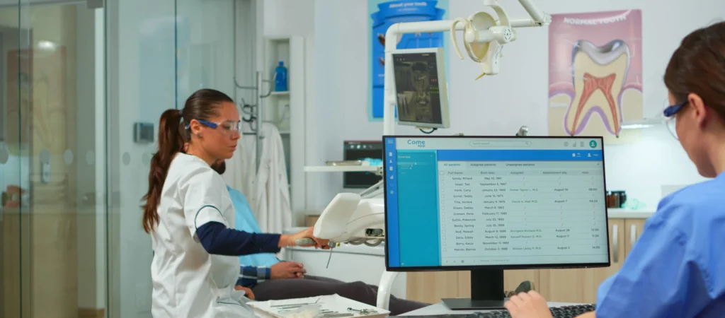 nurse-typing-computer-making-appointments-while-dental-specialist-talking-patient-stomatology-chair-before-examination-dentist-nurse-working-together-modern-stomatological-clinic